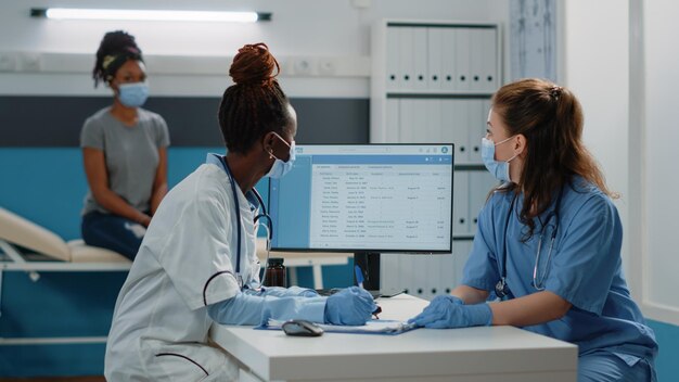 Equipo de médicos y enfermeras que preparan el papel de prescripción para el paciente en la visita de control anual. Grupo de especialistas médicos que hablan sobre tratamientos curativos y medicamentos durante la pandemia