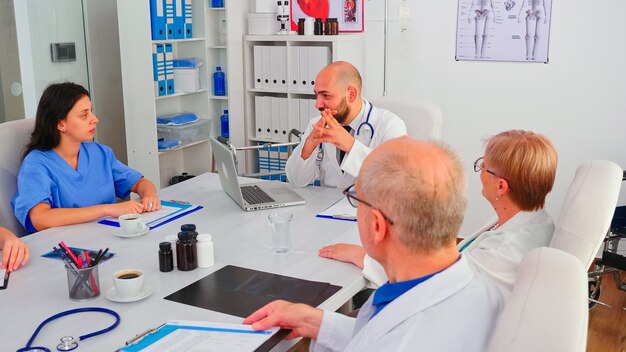 Equipo de médicos con sesión de lluvia de ideas sentados en el escritorio en la sala de conferencias del hospital. Terapeuta experto de la clínica hablando con sus colegas sobre la enfermedad, los síntomas de la enfermedad en el consultorio médico