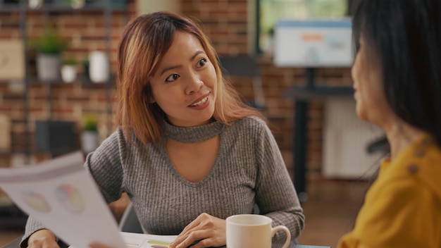 Equipo de mujeres asiáticas analizando estadísticas de ventas sobre papeleo, creando presentaciones de comercio electrónico para el desarrollo. Compañeros de trabajo que planean inversiones financieras y lluvia de ideas sobre ideas estratégicas.