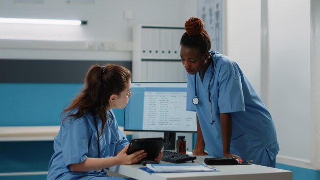 Equipo multiétnico de enfermeras mirando tableta digital para consulta y tratamiento. Grupo diverso de asistentes médicos que trabajan con tecnología para el sistema de salud y el chequeo.