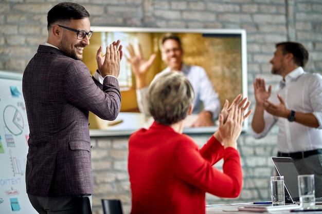 Equipo de negocios feliz aplaudiendo mientras tiene una videoconferencia con su colega en la oficina