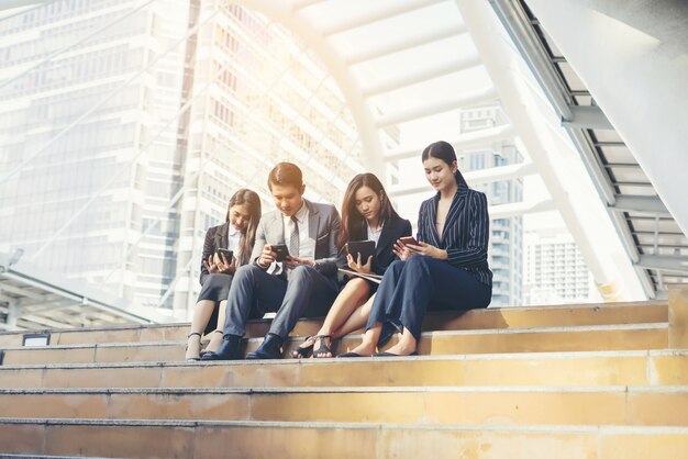 Equipo de negocios tomar un se sienta en los pasos con el teléfono inteligente.