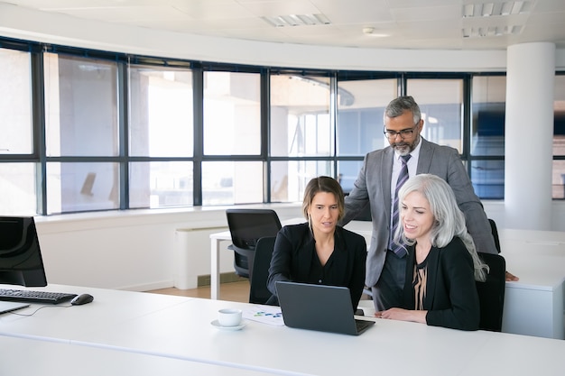 Equipo de negocios de tres viendo la presentación en el monitor de la PC, discutiendo el proyecto, sentado en el lugar de trabajo y apuntando a la pantalla. Copie el espacio. Concepto de reunión de negocios