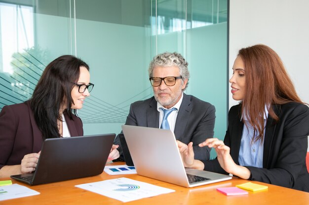 Equipo de negocios usando computadoras mientras analiza el diagrama en la reunión corporativa en la mesa.