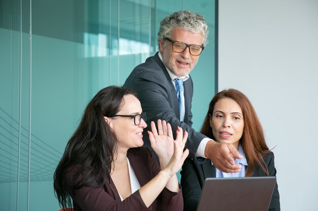 Equipo de negocios viendo y discutiendo la presentación en la computadora portátil, ejecutivo masculino apuntando a la pantalla