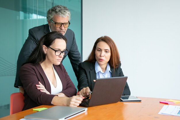 Equipo de negocios viendo la presentación en la computadora portátil, apuntando a la pantalla, discutiendo los detalles