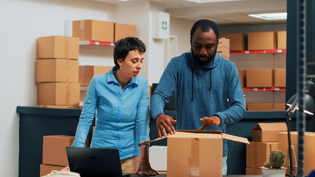 Foto gratuita equipo de propietarios haciendo un gesto alto después de preparar el pedido del almacén, trabajando juntos para enviar mercancías y hacer control de calidad. hombre y mujer que planean el envío de productos. disparo de trípode.