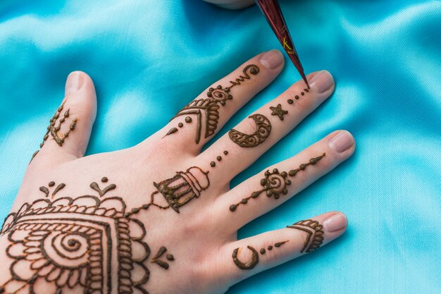 Equipo para tatuar mehndi se acerca a mano de mujer.