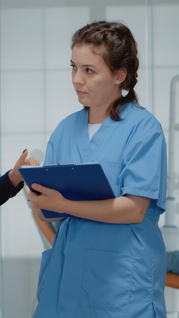 Equipo de trabajo de ortodoncistas discutiendo la operación dental en la clínica. Dentista y asistente de pie en el gabinete estomatológico mientras hablan sobre el equipo bucal y el examen de los dientes