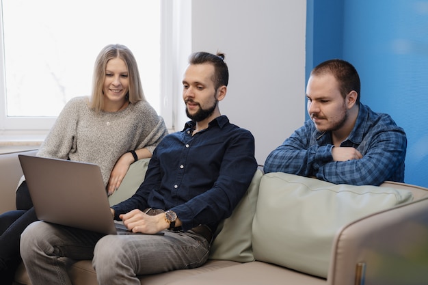 Equipo de tres personas que trabajan en la computadora portátil en la oficina en el sofá