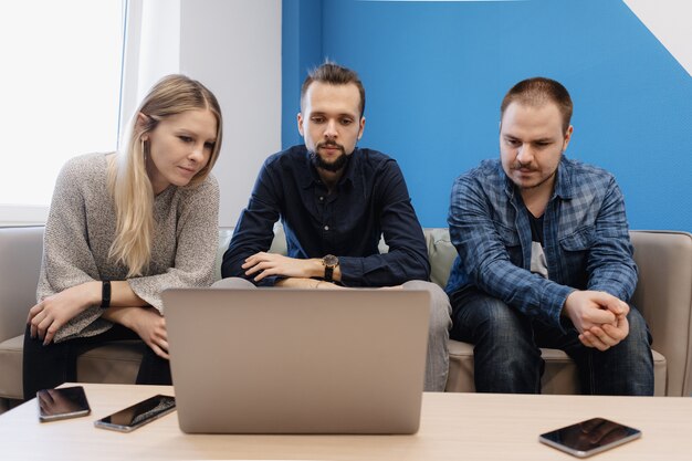 Equipo de tres personas que trabajan en la computadora portátil en la oficina en el sofá