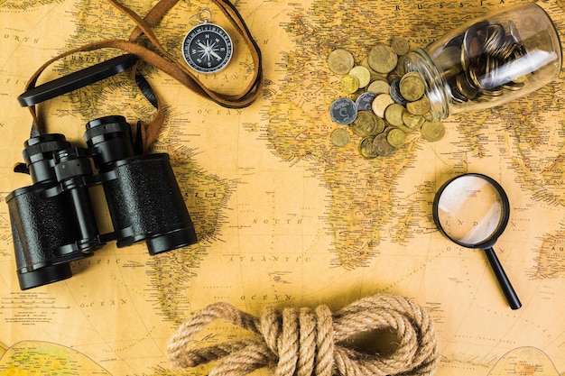Equipos de viaje y jarra de vidrio con monedas en el mapa de la vendimia