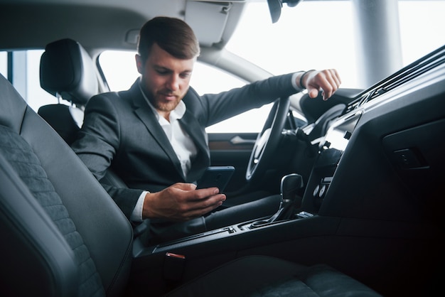 Es hora de detenerse y tomar un descanso. Hombre de negocios moderno probando su nuevo coche en el salón del automóvil