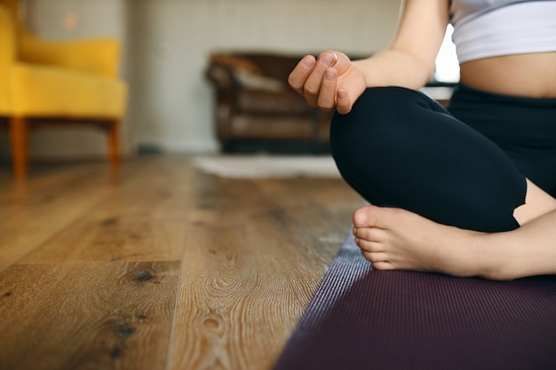 Foto gratuita es hora de ir más despacio. imagen recortada de irreconocible joven mujer descalza practicando meditación durante el yoga, sentada en la estera con las piernas cruzadas.