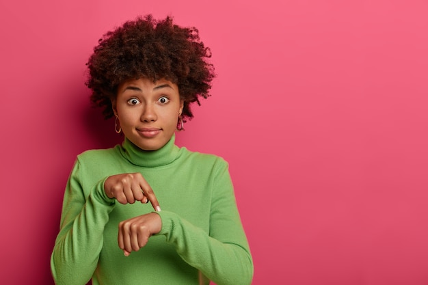 Foto gratuita es hora de irse, ¡apúrate! mujer étnica sorprendida señala la muñeca, hace un gesto de tiempo, muestra que debemos hacer todo rápidamente