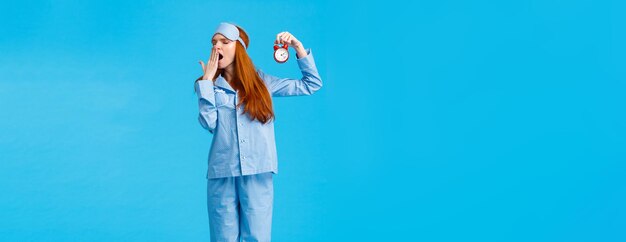 Foto gratuita es tan tarde para acostarse cansada y somnolienta linda mujer pelirroja en ropa de dormir y antifaz para dormir con rojo