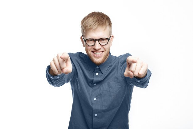 Es tu oportunidad. Hombre joven sin afeitar confiado hermoso en anteojos elegantes y camisa marrón señalando con el dedo índice, eligiéndote, sonriendo con entusiasmo, posando