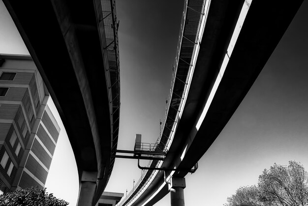Escala de grises de ángulo bajo de un puente de hormigón bajo la luz del sol durante el día