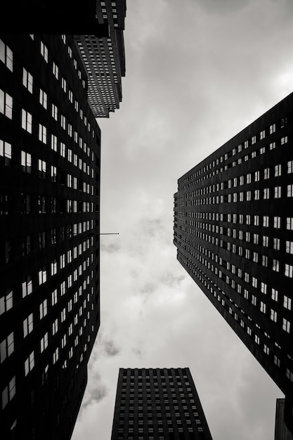 Escala de grises de ángulo bajo vertical de edificios de la ciudad con un cielo nublado en el fondo