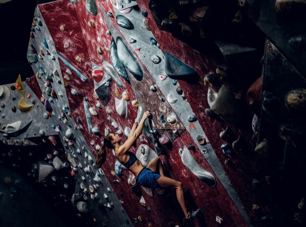 Escalador femenino profesional en una pared de búlder en el interior.