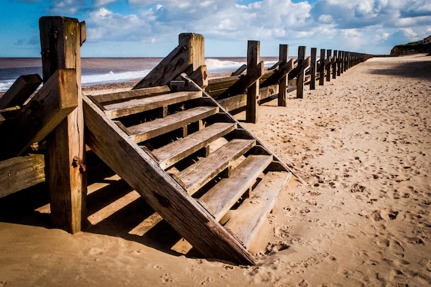 Escalera de madera sobre la valla en una playa de arena bajo el hermoso cielo