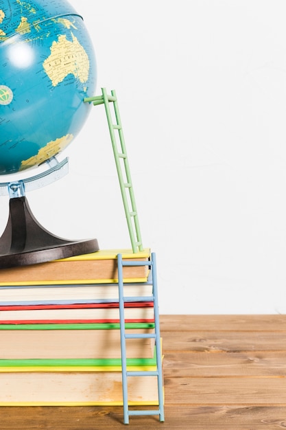 Foto gratuita escalera de papel en el mapa global terrestre soporte bola y libros sobre mesa de madera