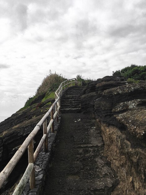 Escalera de piedra hacia la cima de la colina con barandilla de madera bajo cielo nublado gris después de la lluvia