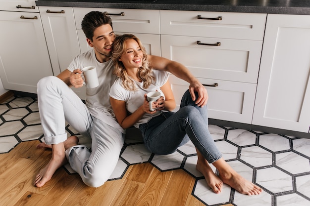 Foto gratuita escalofriantes jóvenes tomando café en la mañana del fin de semana retrato interior de pareja sonriente relajante durante el desayuno.