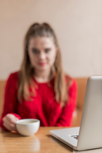 Escena borrosa de mujer con portátil y taza de café