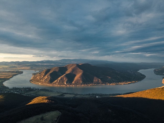 Escena fascinante de un río entre el bosque y la colina bajo el cielo nublado