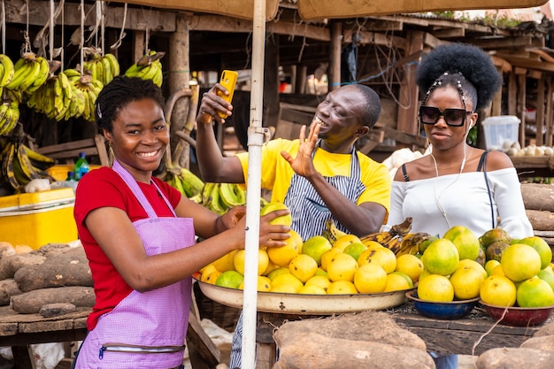 Escena del mercado local con comerciantes felices vendiendo, uno usando su teléfono para hacer videollamadas