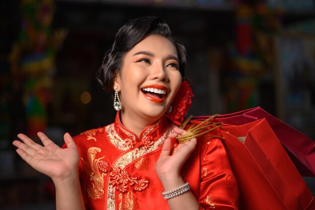 Escena nocturna, retrato hermosa mujer asiática vistiendo un cheongsam sonriendo y posa con bolsas de compras en el santuario en el año nuevo chino