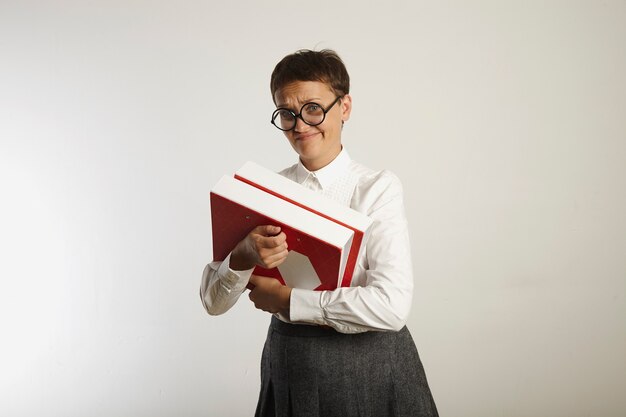 Escéptica profesora vestida de forma conservadora sosteniendo carpetas brillantes pesadas en blanco