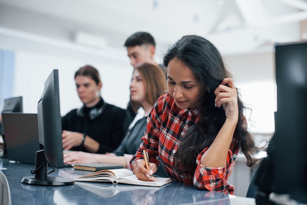 Escribiendo en el bloc de notas. Grupo de jóvenes en ropa casual que trabajan en la oficina moderna