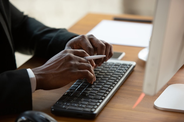 Escribiendo texto, de cerca. Emprendedor afroamericano, empresario que trabaja concentrado en la oficina. Se ve seria y ocupada, vistiendo traje clásico.