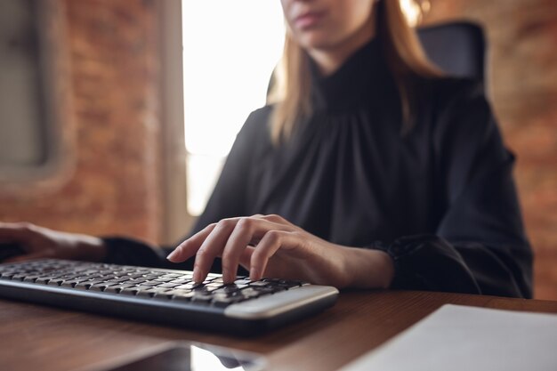 Escribiendo texto, de cerca. Mujer joven caucásica en traje de negocios trabajando en oficina. Joven empresaria, gerente haciendo tareas con teléfono inteligente, computadora portátil, tableta tiene conferencia en línea. Finanzas, trabajo.