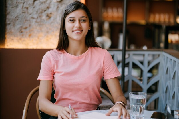 Escribir productos lácteos en nota en la cafetería, concepto como memoria de la vida. Mujer en cafetería. Mujer sonriente haciendo el bloc de notas.