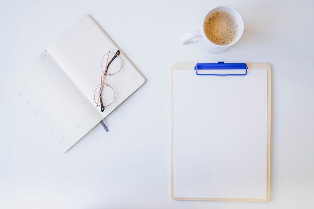 Escritorio blanco con carpeta, gafas y café