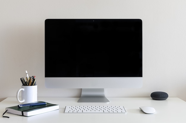 Escritorio con una computadora, una taza con bolígrafos y lápices contra una pared blanca