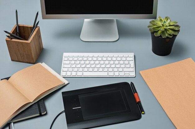 El escritorio gris con laptop, bloc de notas con hoja en blanco, maceta de flores, lápiz y tableta para retocar