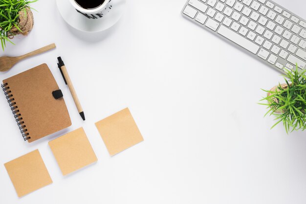 Escritorio de negocios blanco con diario; notas adhesivas; Taza de café y teclado en el escritorio blanco