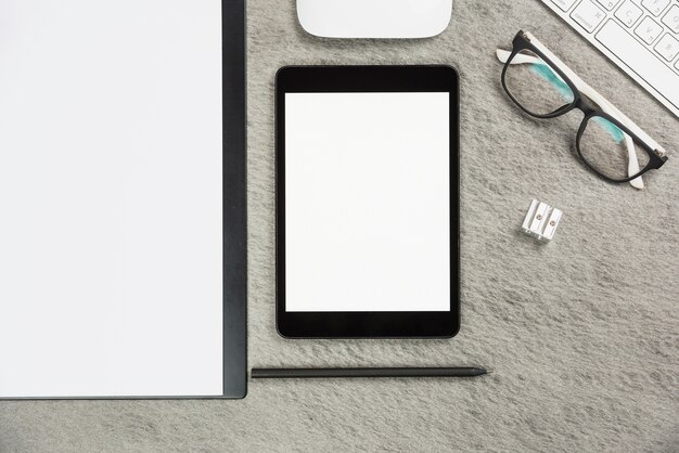 Escritorio de oficina gris con portapapeles; tableta digital; lápiz; sacapuntas; ratón; teclado y anteojos