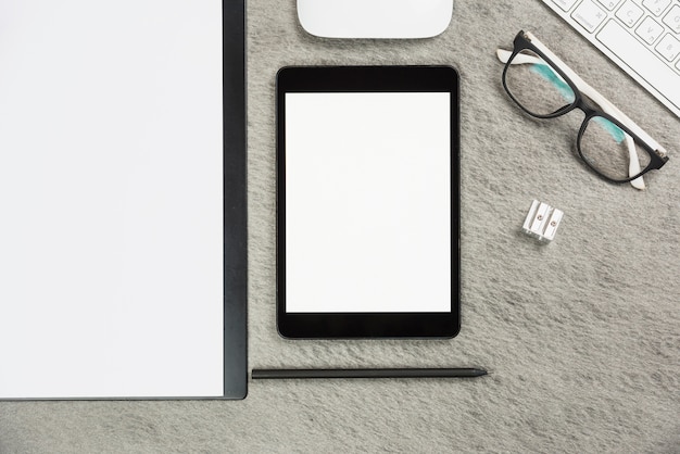 Escritorio de oficina gris con portapapeles; tableta digital; lápiz; sacapuntas; ratón; teclado y anteojos