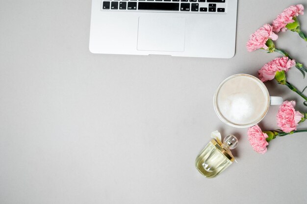 Escritorio de oficina plano para mujer Espacio de trabajo con papelería de clavel rosa para computadora portátil en la mesa blanca Vista superior