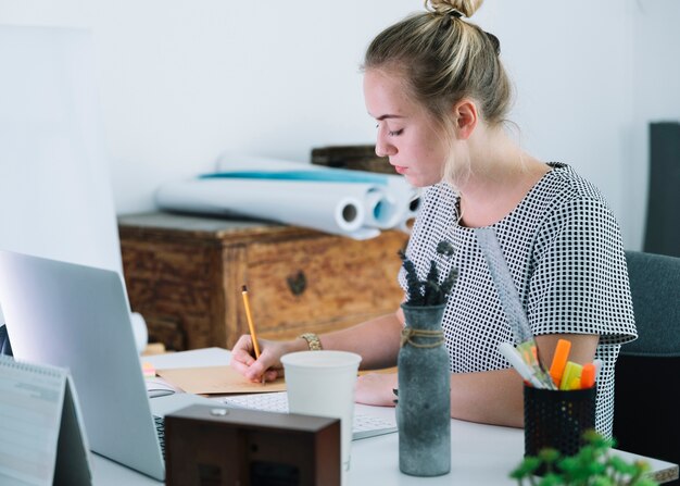 Escritura joven de la empresaria en el papel sobre el escritorio