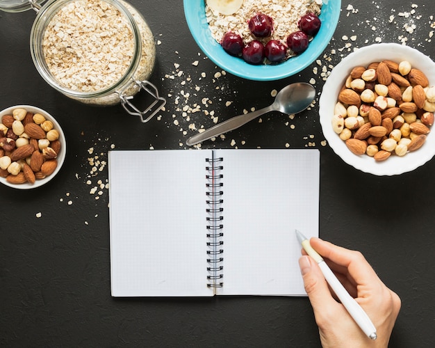 Escritura a mano en el cuaderno cerca de nueces mix y avena jar