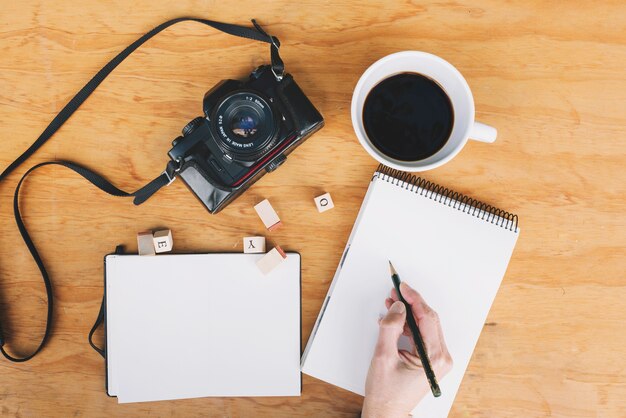 Escritura de la mano de cultivo en el cuaderno cerca de la cámara y el café