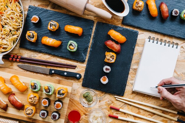 Escritura de la mano de cultivo en el cuaderno cerca de sushi