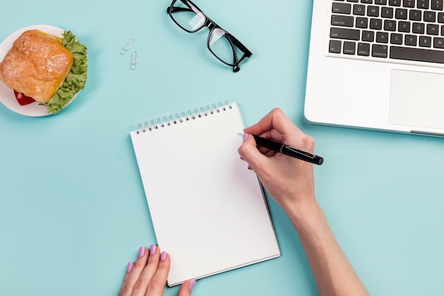 Escritura de la mano de la empresaria en la libreta espiral con la pluma sobre el escritorio de oficina