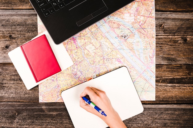 Escritura de la mano de la persona en el bloc de notas con diario y mapa en la mesa de madera